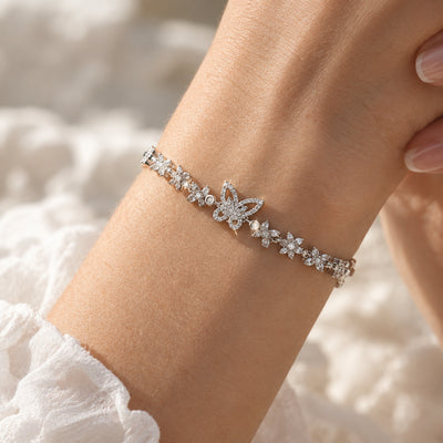 Silver Bloom & Butterfly Bracelet — Silver-tone link chain with a pavé crystal butterfly and floral charms (close-up detail)