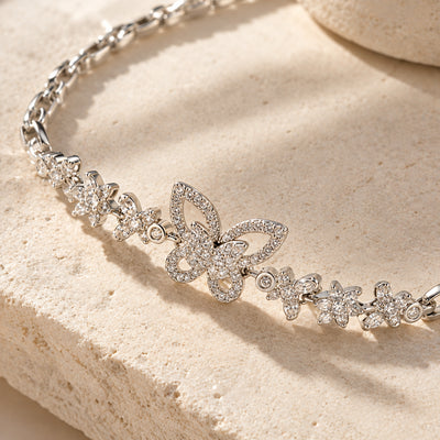 Silver Bloom & Butterfly Bracelet — Silver-tone link chain with a pavé crystal butterfly and floral charms (styled on model)